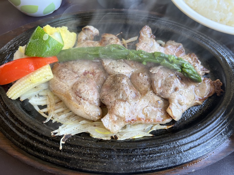 鉄板焼。肉に、赤ピーマン、プチとうもろこし、アスパラガス、ズッキーニなどが乗っている写真