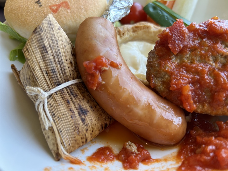 ソーセージの後ろに竹の葉で包まれたおこわ(ちまき)がある写真